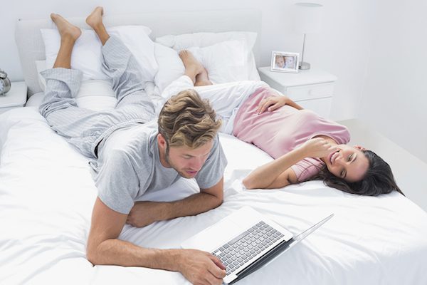 Man using a laptop next to his wife lying